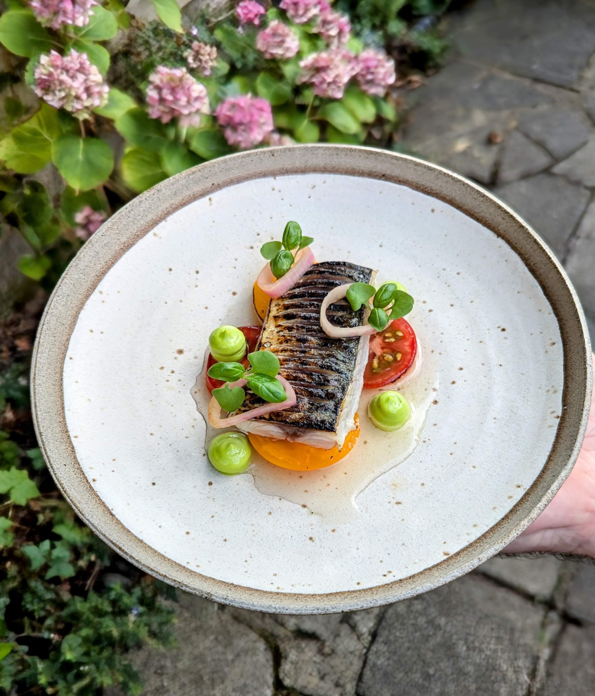 A gourmet seafood dish meticulously plated with vibrant seasonal vegetables and a light foam garnish.